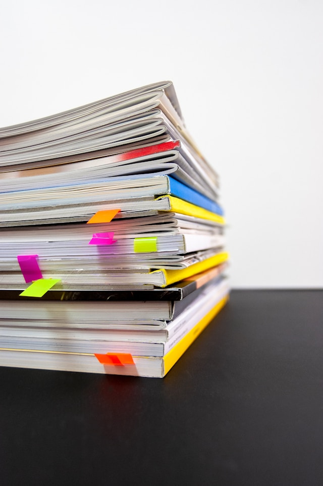 A stack of paper marketing reports on a desk with multicolour tabs on important pages.